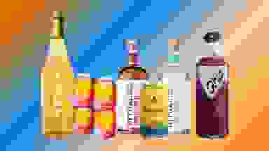 Non-alcoholic wine, mixers, beer, spirits, and cocktails are arranged in a row over a colorful blue and orange gradient background.